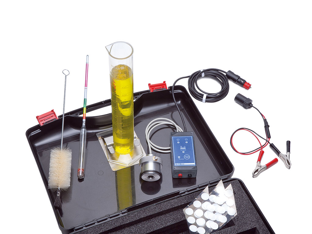 Werkzeuge – Qualität für Profis Das Kraftstoff-Identifikations-Kit - KIK 01_LR enthält einen Messzylinder mit gelber Flüssigkeit, Drähte, eine Bürste, ein Thermometer und andere Ausrüstung, praktisch untergebracht in einem offenen schwarzen Koffer. Es ist ideal für angehende Wissenschaftler, die vielleicht auch ein Schraubenschlüssel-Set erwerben möchten, um ihr Projekt-Toolkit zu erweitern. Jetzt kaufen