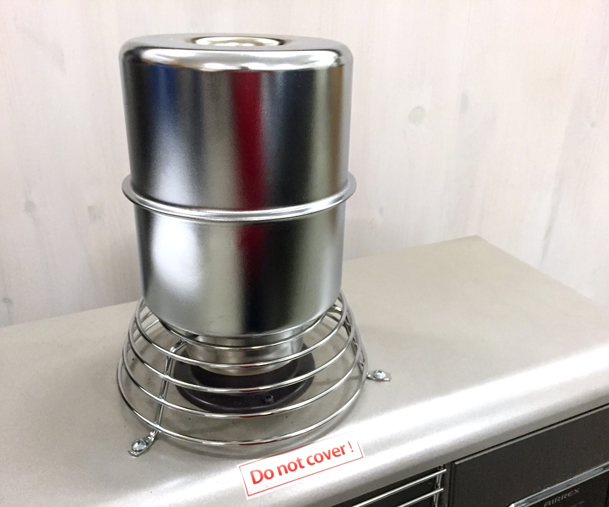 Werkzeuge – Qualität für Profis Das Metallheizgerät AIRREX AH-10106 mit Schutzkorb wird auf eine Fläche gestellt; ein rot-weißes Etikett mit der Aufschrift "Nicht abdecken" befindet sich davor. Jetzt kaufen