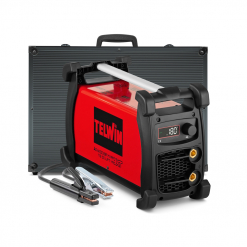 Werkzeuge – Qualität für Profis Ein rot-schwarzes TELWIN ADVANCE 227 XT MV/PFC VRD-Schweißgerät ist mit angeschlossenen Kabeln und einem schwarzen Tragekoffer dahinter abgebildet. Auf der Vorderseite sind eine LED-Anzeige und ein Bedienknopf zu sehen. Jetzt kaufen