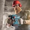 Werkzeuge – Qualität für Profis Ein Mann in Schutzkleidung bearbeitet mit einer Bohrmaschine eine Betonwand in einer Industrieumgebung. Jetzt kaufen