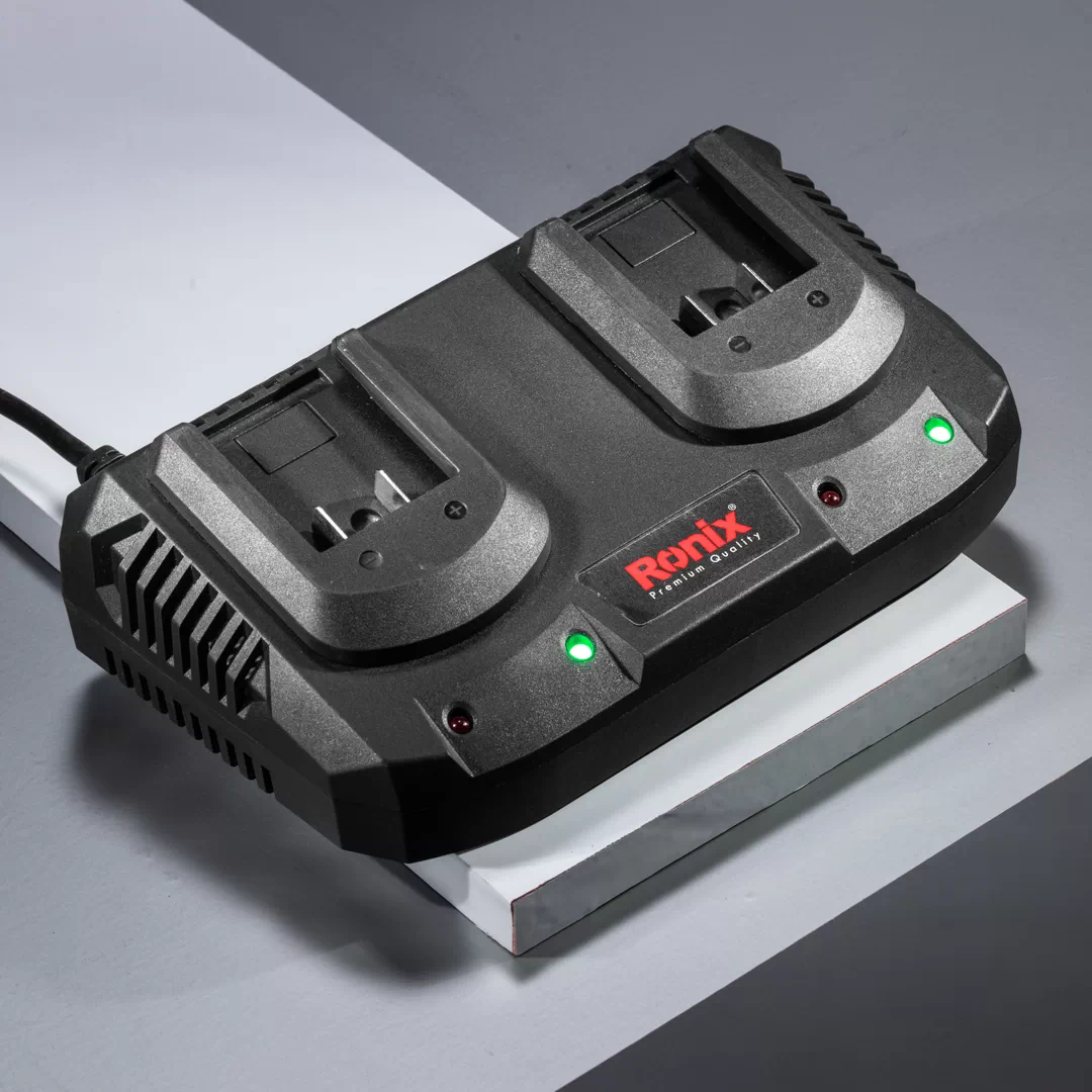 Werkzeuge – Qualität für Profis Schwarzes Ronix-Doppelbatterieladegerät mit zwei Steckplätzen, zwei grünen Kontrollleuchten und angeschlossenem Stromkabel, platziert auf einer grau-weißen Fläche. Jetzt kaufen