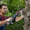 Werkzeuge – Qualität für Profis Eine Person, die eine Schutzbrille und Handschuhe trägt, schneidet im Freien mit einer akkubetriebenen Kettensäge der Marke Ronix einen toten Ast ab. Jetzt kaufen