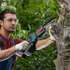 Werkzeuge – Qualität für Profis Eine Person, die eine Schutzbrille und Handschuhe trägt, schneidet im Freien mit einer akkubetriebenen Kettensäge der Marke Ronix einen toten Ast ab. Jetzt kaufen