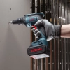 Werkzeuge – Qualität für Profis Eine Hand in einem Handschuh schraubt mit einer blauen, akkubetriebenen Ronix-Bohrmaschine eine Schraube in eine graue Wand, im Hintergrund sind Metallstangen zu sehen. Jetzt kaufen