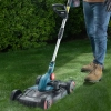 Werkzeuge – Qualität für Profis Eine Person, die einen akkubetriebenen Rasenmäher auf grünem Rasen in der Nähe einer Hecke benutzt und dabei blaue Jeans und braune Stiefel trägt. Jetzt kaufen