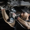 Werkzeuge – Qualität für Profis Eine Person, die eine Schutzbrille und Handschuhe trägt, arbeitet mit einer Akku-Bohrmaschine an der Unterseite eines Fahrzeugs. Jetzt kaufen