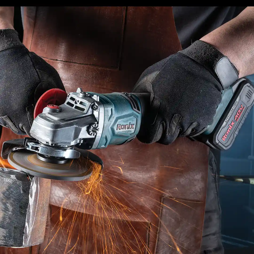 Werkzeuge – Qualität für Profis Eine Person, die schwarze Handschuhe und eine braune Schürze trägt, schneidet mit einem RONIX-Winkelschleifer Metall und erzeugt dabei leuchtend orangefarbene Funken. Jetzt kaufen