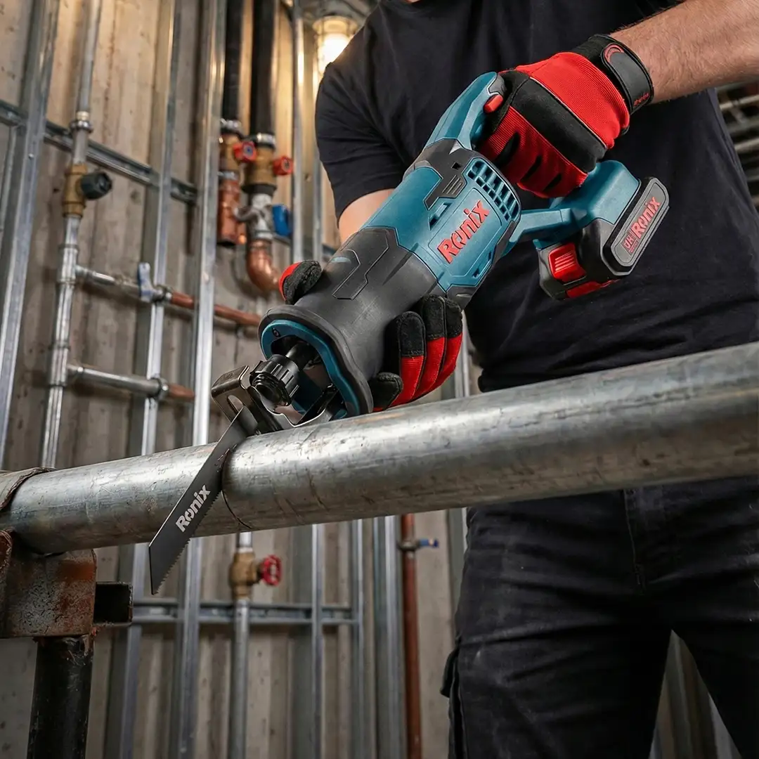 Werkzeuge – Qualität für Profis Eine Person, die Arbeitshandschuhe trägt, schneidet mit der RONIX Akku-Säbelsäge 8621 ein Metallrohr in einer industriellen Umgebung, in der Rohre und Ventile offen liegen. Jetzt kaufen